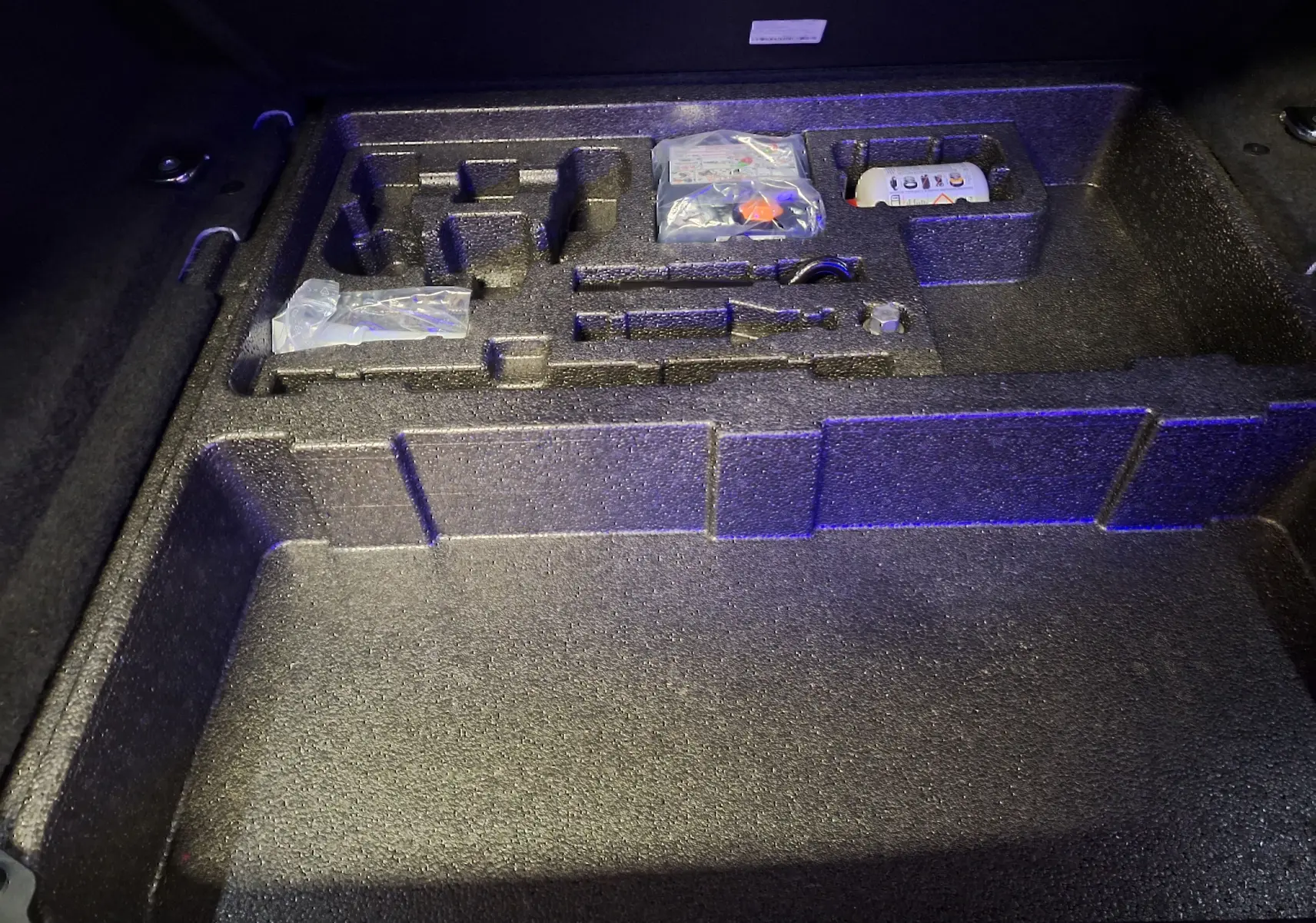 Rangement en mousse dans le coffre du Jaguar E-PACE blanc, compartiments pour outils et accessoires visibles.