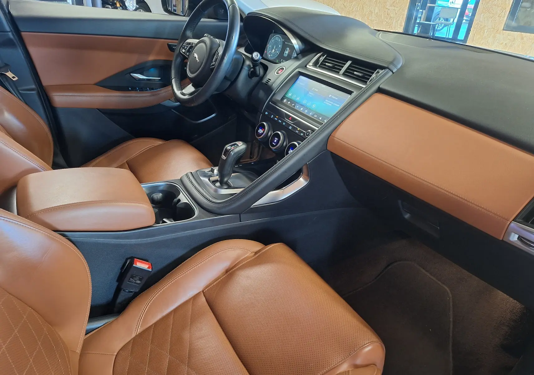 Intérieur Jaguar E-PACE 2019 vu côté passager, sièges cuir marron et tableau de bord noir avec écran tactile central.