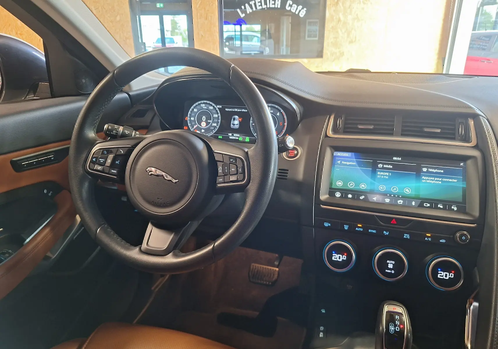 Intérieur du Jaguar E-PACE blanc 2019, vue du poste de conduite avec volant cuir et écran tactile central.