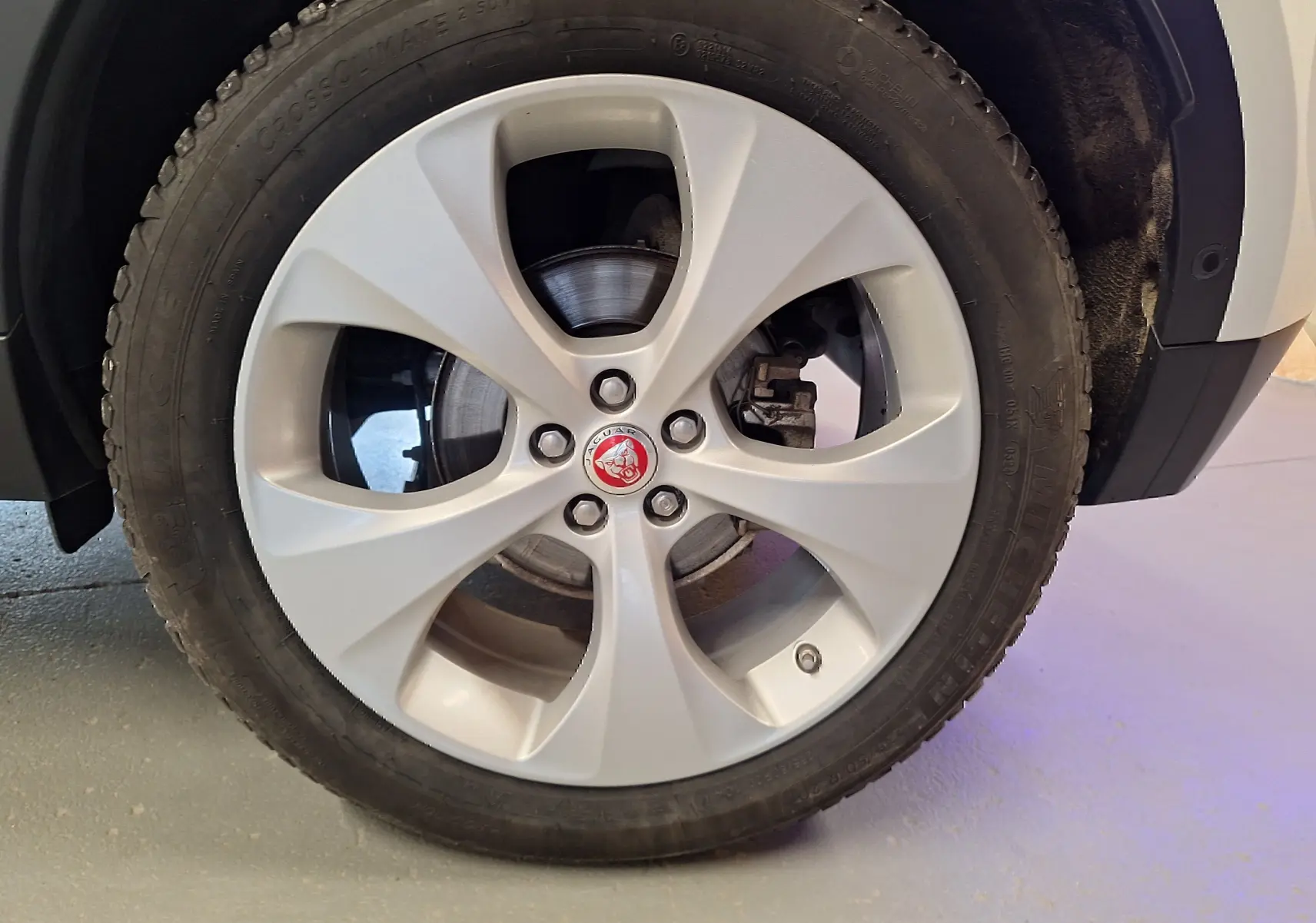 Gros plan sur la roue avant droite du Jaguar E-PACE blanc, mettant en valeur la jante argentée et le logo Jaguar central.