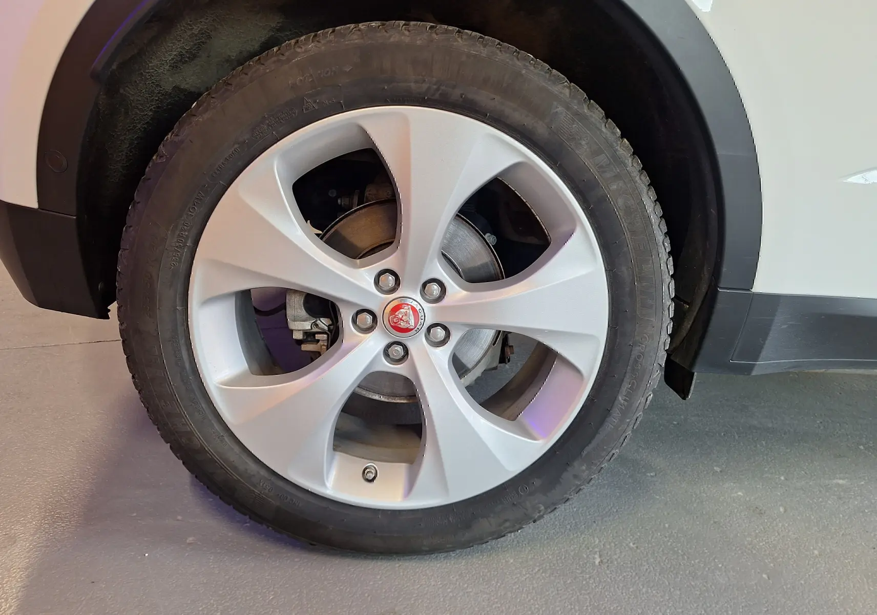 Gros plan sur la roue avant droite du Jaguar E-PACE blanc, avec jante argentée et logo Jaguar rouge au centre.