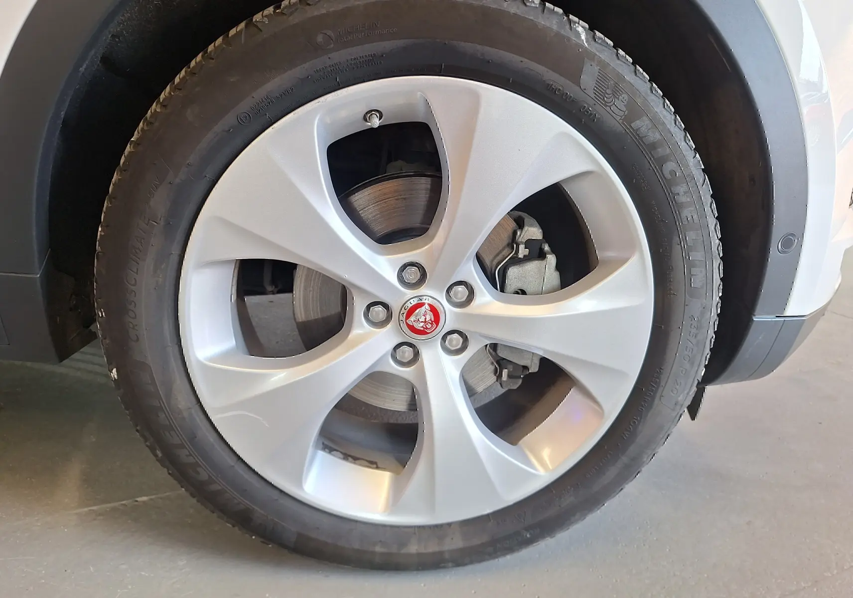 Gros plan sur la roue avant droite du Jaguar E-PACE blanc 2019 avec jante argentée et logo Jaguar rouge au centre.