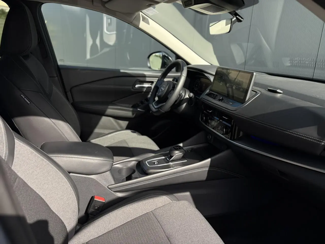 Intérieur du Nissan Qashqai 2025 vu côté conducteur, sièges gris, écran tactile et volant cuir noir.