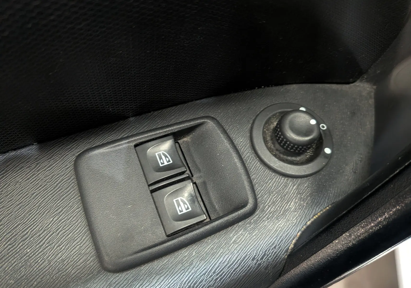 Gros plan sur les commandes électriques des vitres et le réglage des rétroviseurs côté conducteur du Renault Kangoo Express blanc.