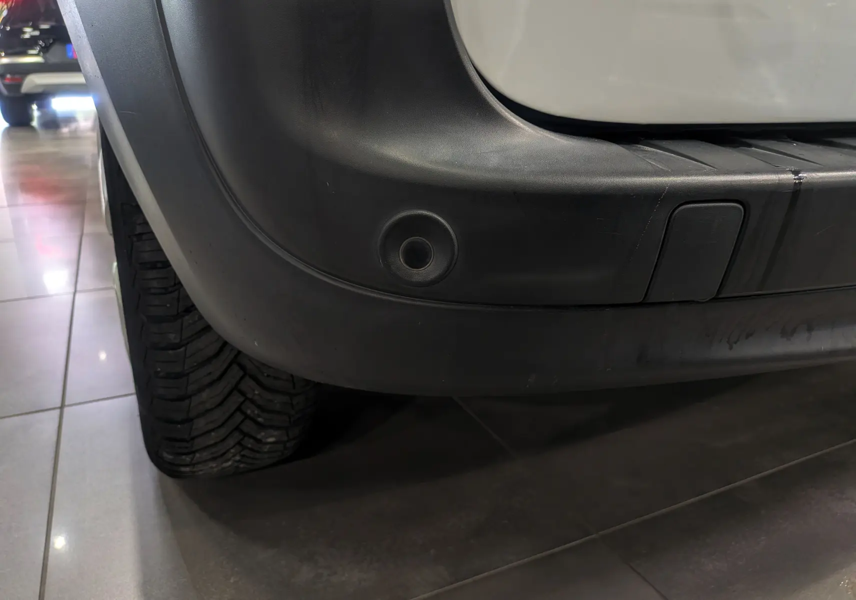 Gros plan sur le pare-chocs arrière droit noir du Renault Kangoo Express blanc minéral, avec capteur de recul visible.