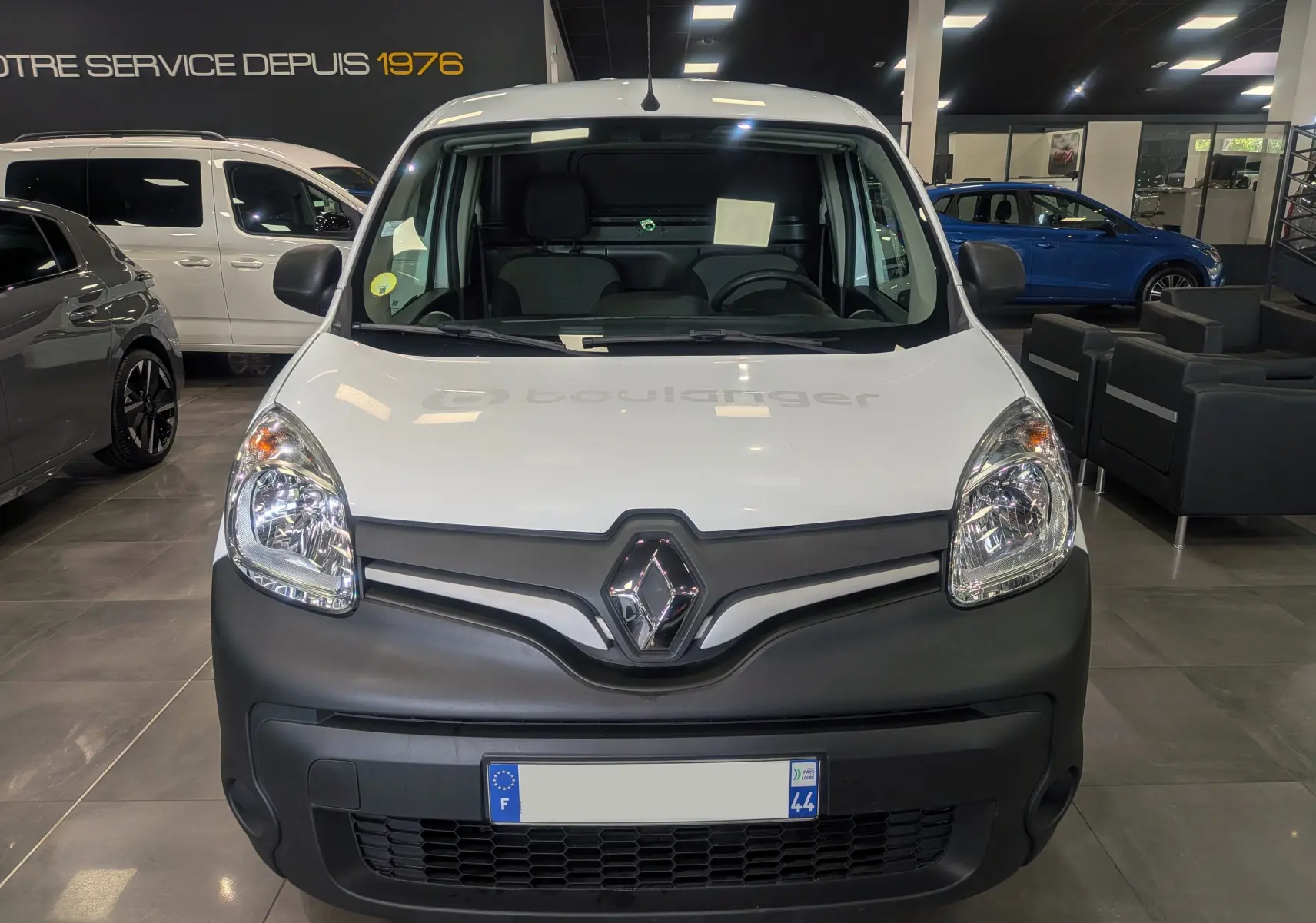 Vue avant d’un Renault Kangoo Express blanc minéral avec pare-chocs noir mat dans un showroom.