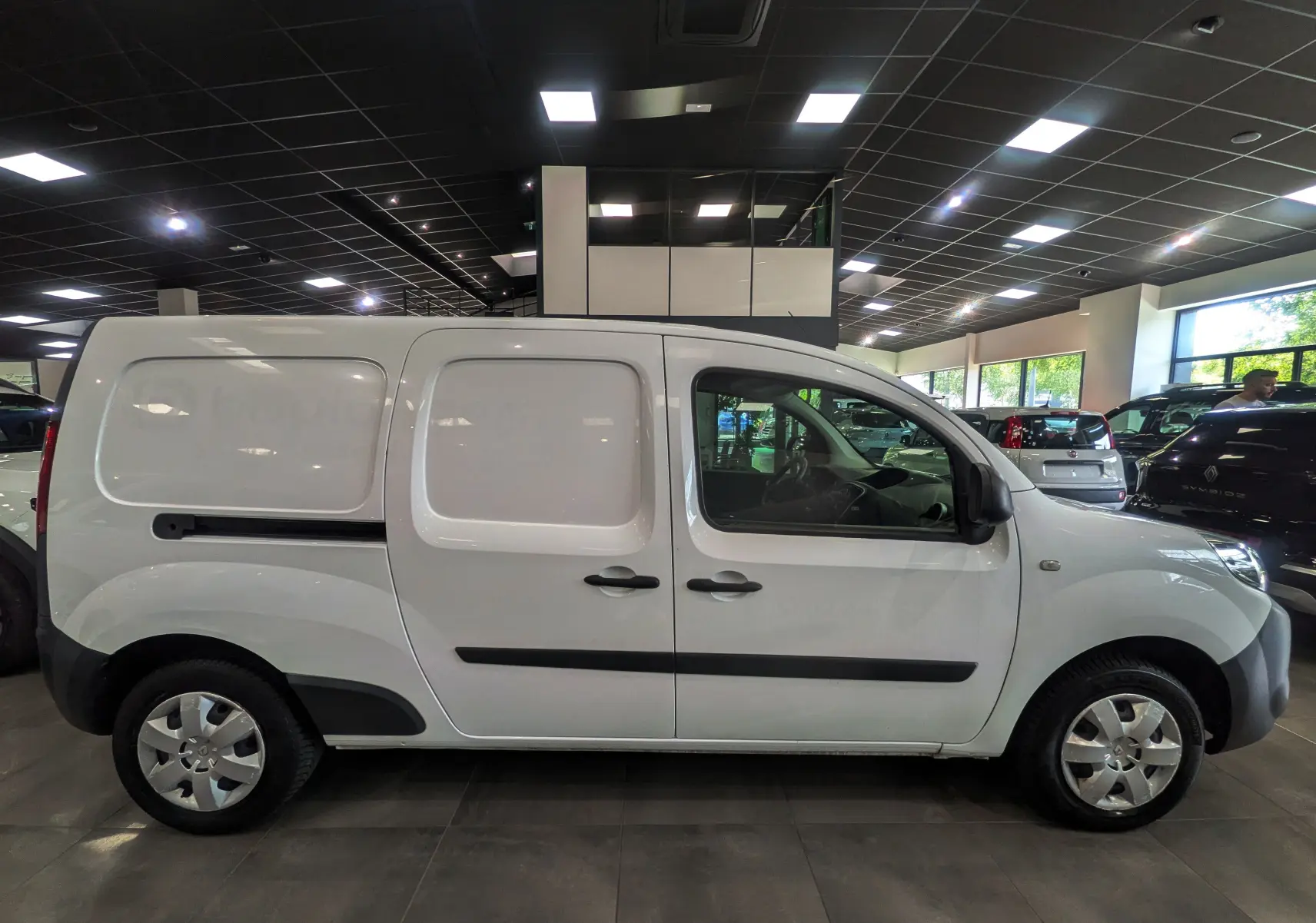 Vue latérale droite d'un Renault Kangoo Express blanc minéral, version Grand Volume, en intérieur showroom.