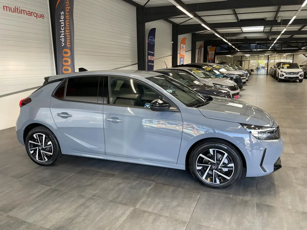 Opel Corsa gris clair vue de profil côté gauche, avec jantes alliage et vitres arrière surteintées.