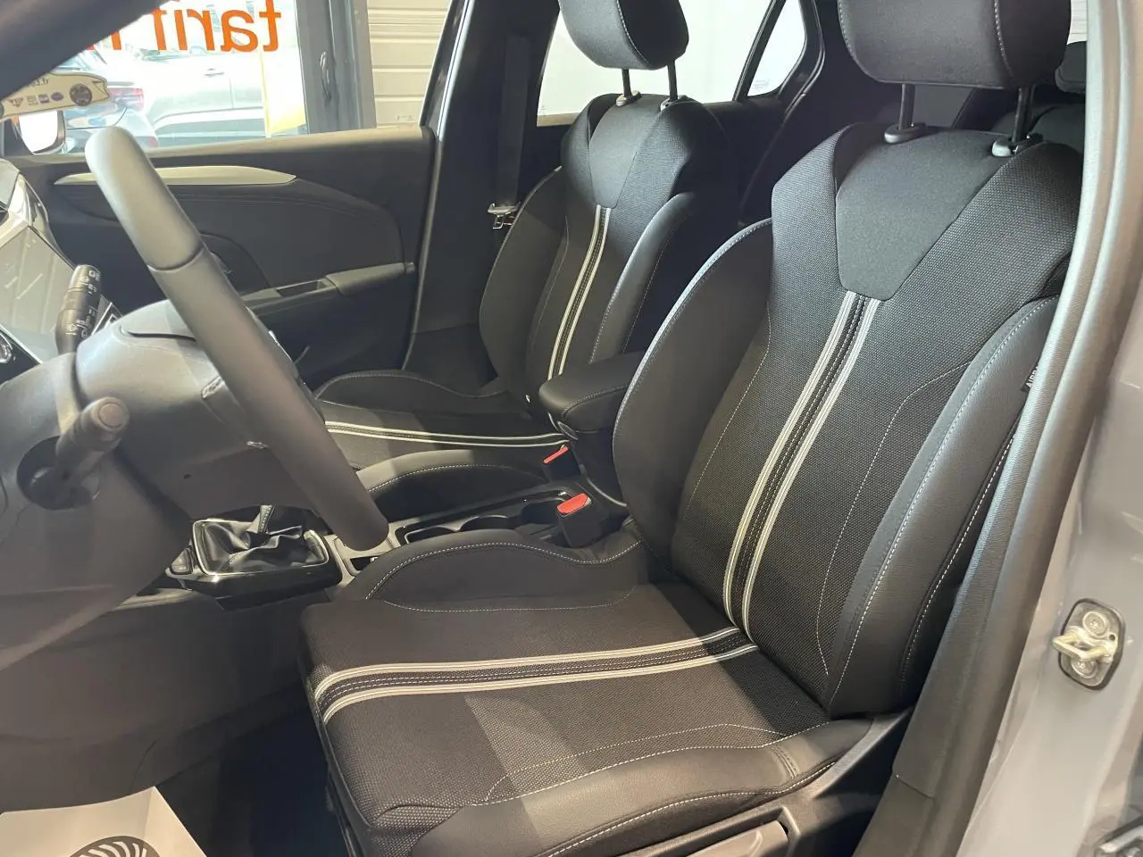 Intérieur avant droit de l’Opel Corsa gris, sièges sport noirs avec bandes blanches et volant cuir synthétique.