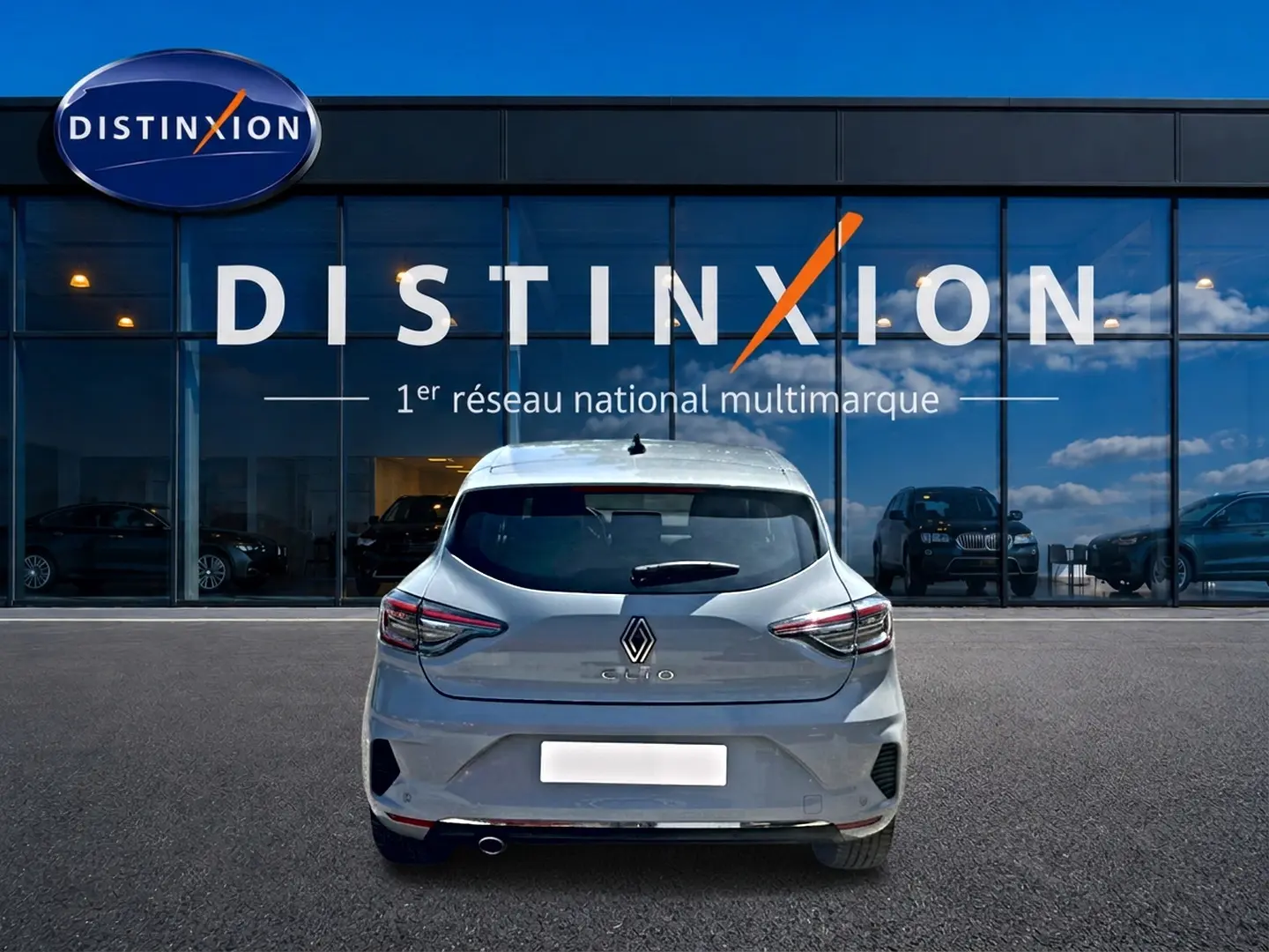 Vue arrière d'une Renault Clio V gris rafale garée devant une vitrine avec logo Distinxion.