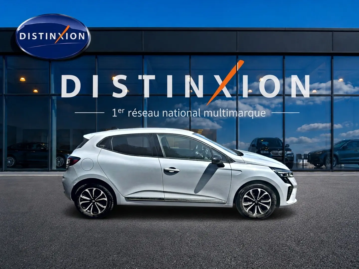 Profil droit d'une Renault Clio V gris rafale avec jantes alu et poignées ton carrosserie devant une vitrine Distinxion.