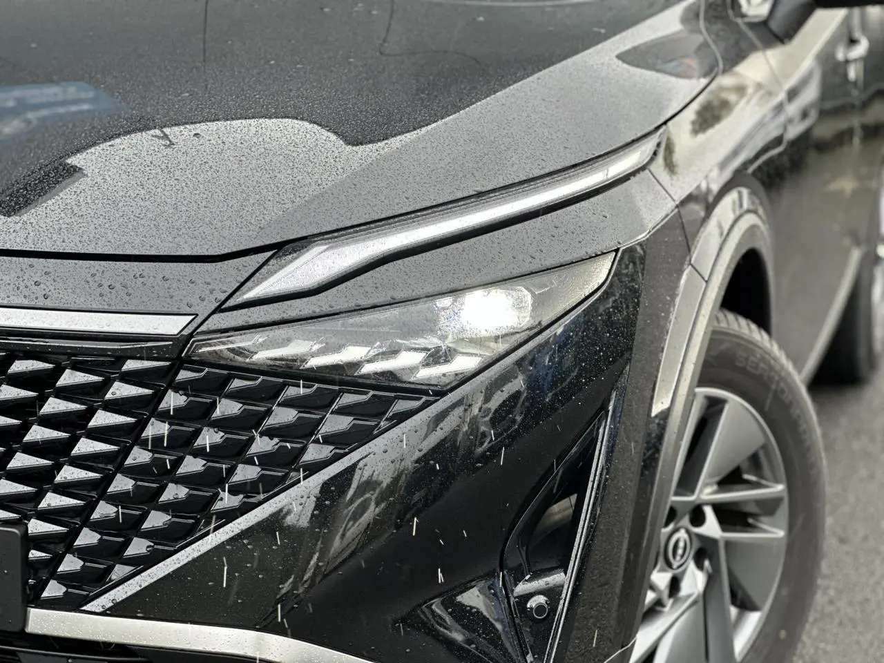 Gros plan sur l'avant droit noir nacré du Nissan Qashqai 2024, mettant en valeur son phare LED et la calandre texturée.