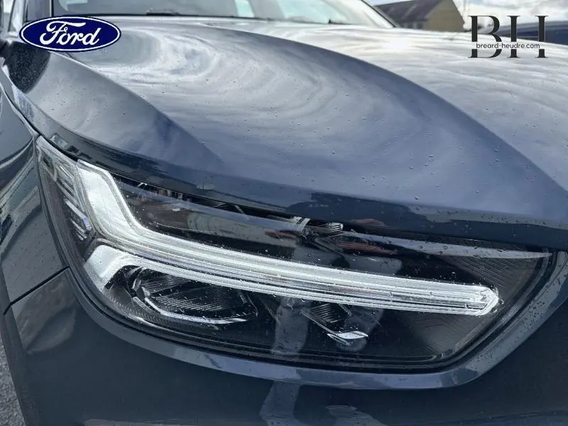 Gros plan sur le phare avant gauche bleu Denim du Volvo XC40 T4 Recharge avec détails LED et carrosserie brillante.