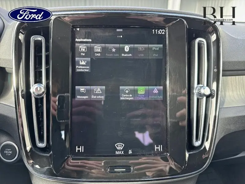 Écran tactile central noir du tableau de bord d'un Volvo XC40 Bleu Denim, avec commandes d'air et interface multimédia visible.