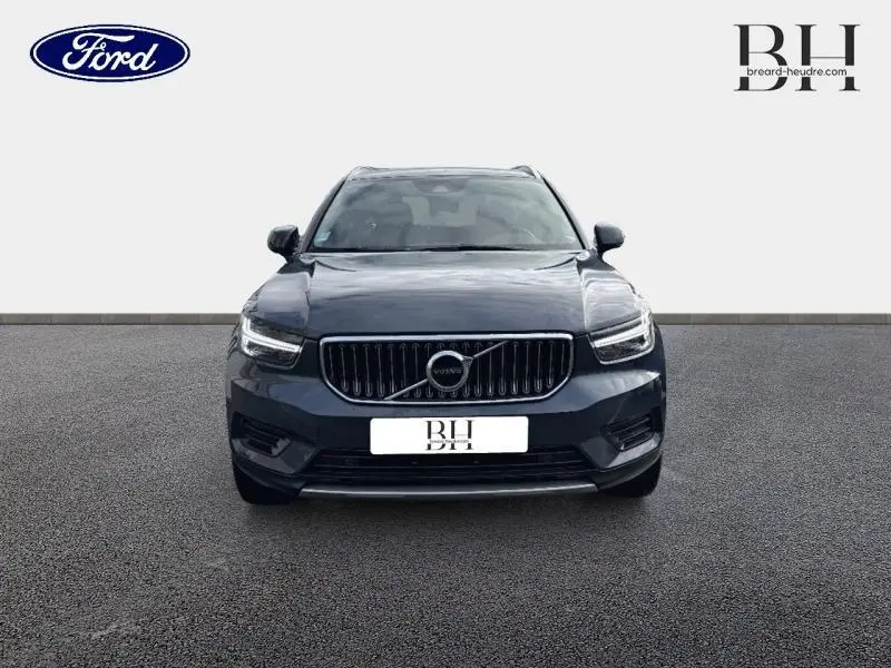 Vue de face d'un Volvo XC40 bleu Denim avec calandre chromée et phares LED allumés sur fond neutre.