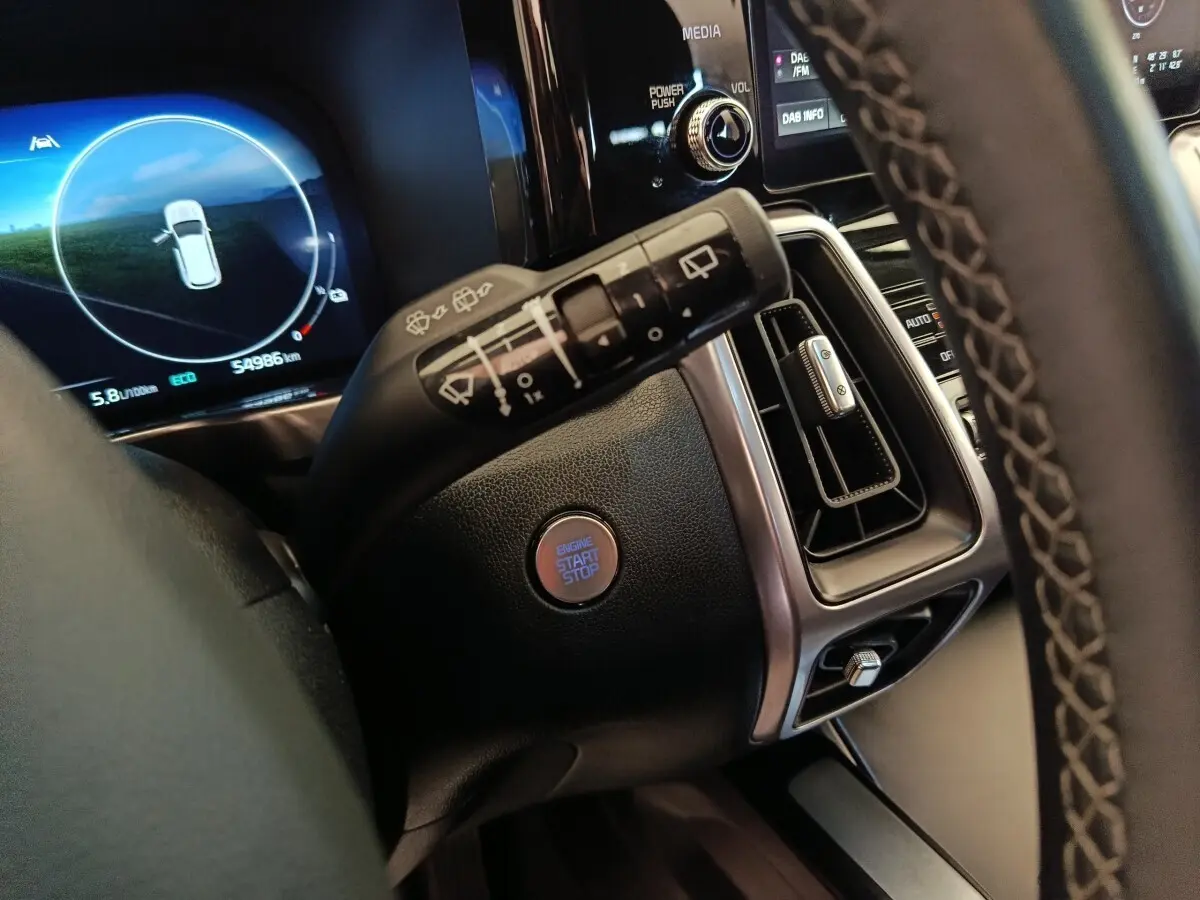 Gros plan intérieur sur la commande d’essuie-glace, bouton start/stop et tableau de bord numérique du Kia Sorento noir 2023.