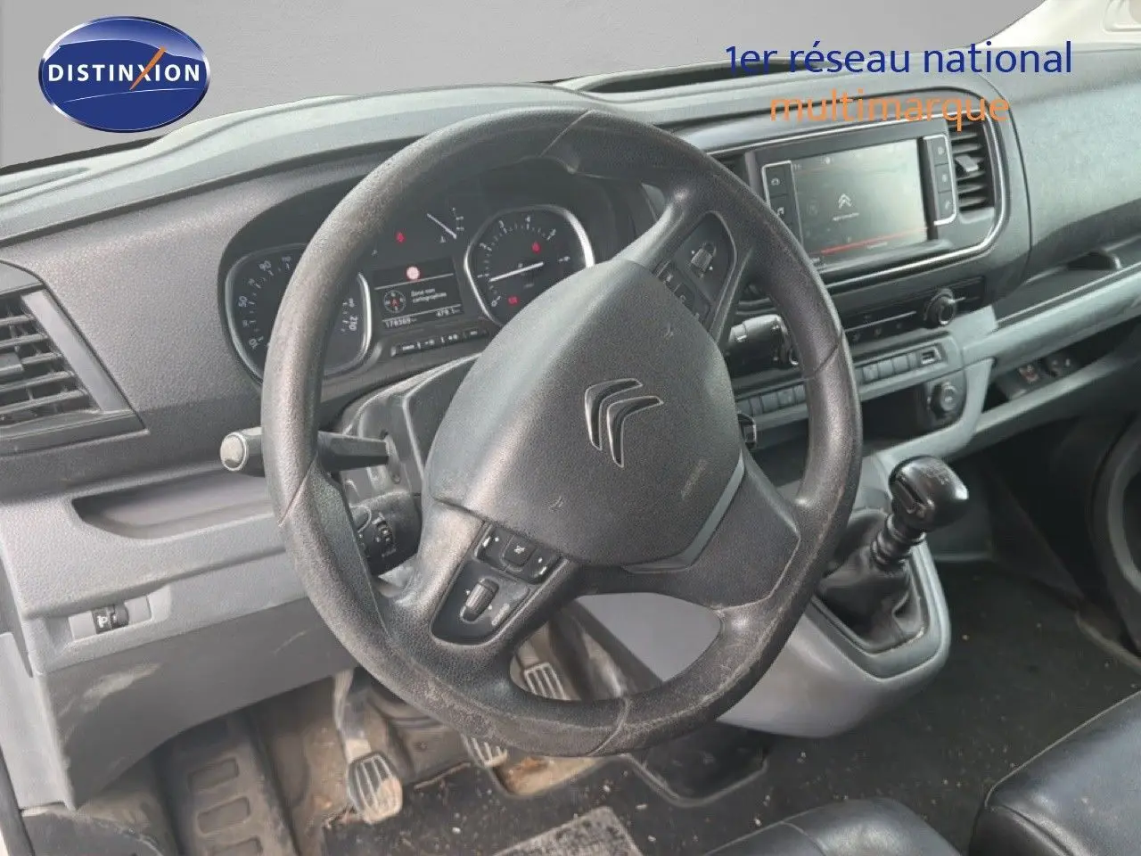 Vue intérieure du poste de conduite du Citroën Jumpy blanc, volant et levier de vitesse manuelle visibles de face.