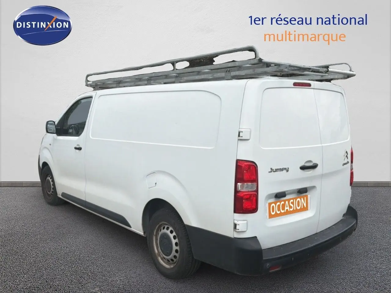Vue 3/4 arrière gauche d’un Citroën Jumpy blanc avec galerie de toit et marquage "occasion" sur la porte arrière.