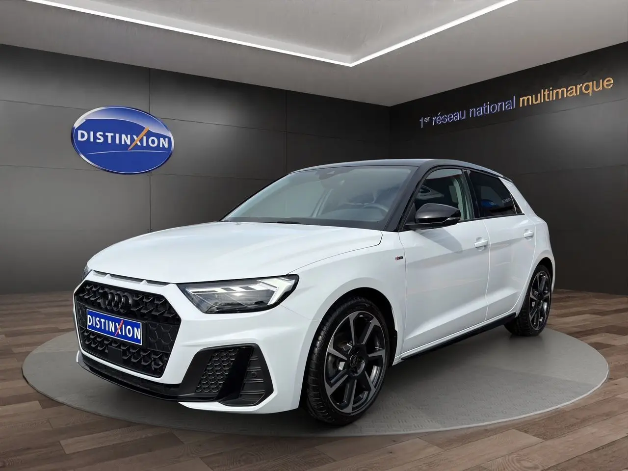 Audi A1 Sportback blanc vue 3/4 avant droit avec toit noir et jantes noires en showroom.