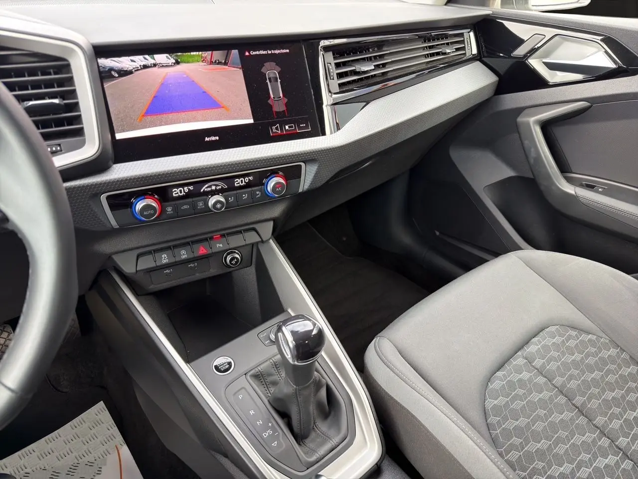 Vue intérieure côté passager de l'Audi A1 Sportback blanche, avec console centrale et écran de caméra de recul allumé.