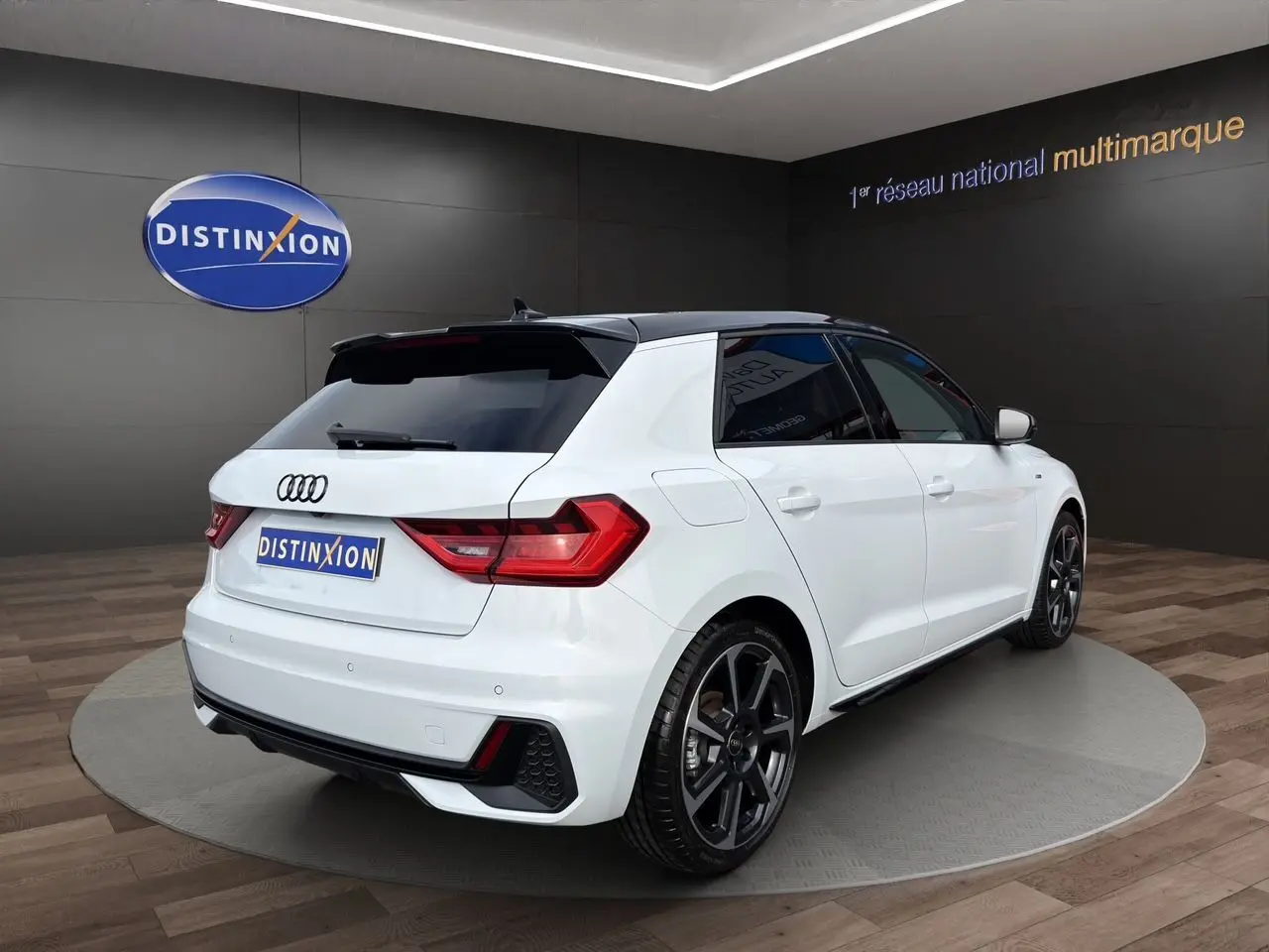 Audi A1 Sportback blanc vue 3/4 arrière droit, avec toit noir et jantes alliage foncé, en showroom.