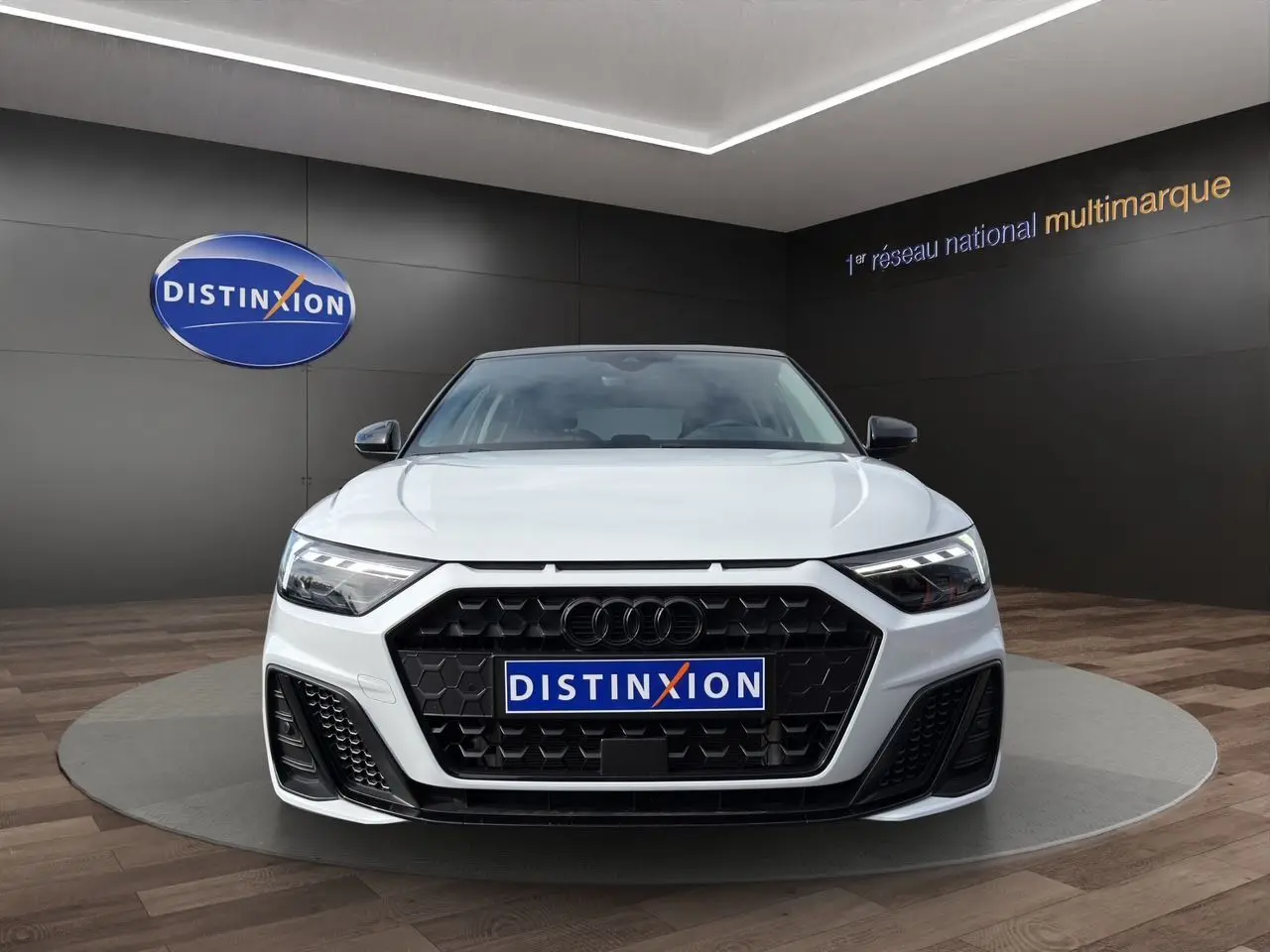 Audi A1 Sportback blanche vue de face, avec calandre noire hexagonale et phares LED distinctifs.