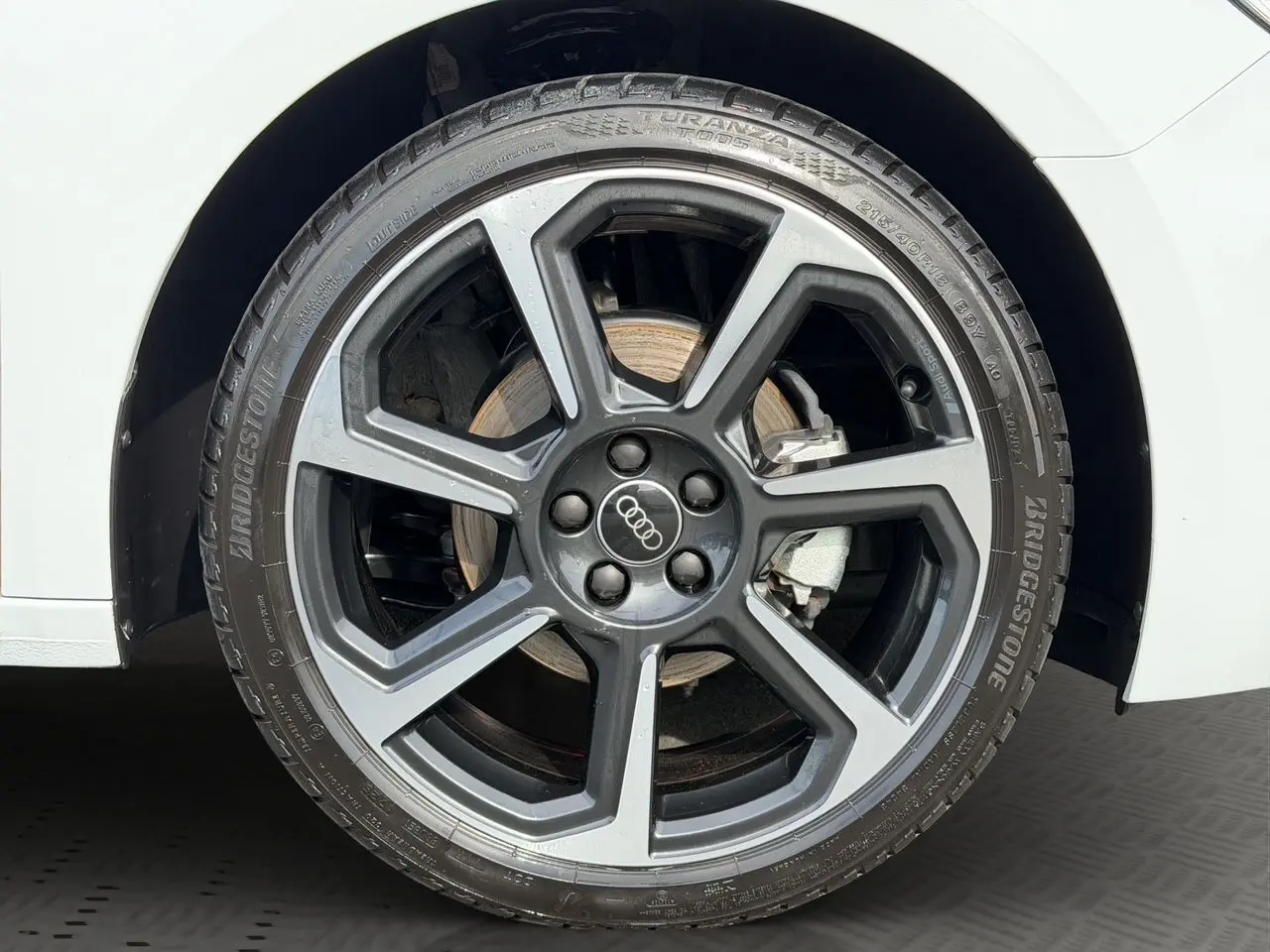 Gros plan sur la roue avant droite d'une Audi A1 Sportback blanche avec jante alliage gris foncé à design moderne.