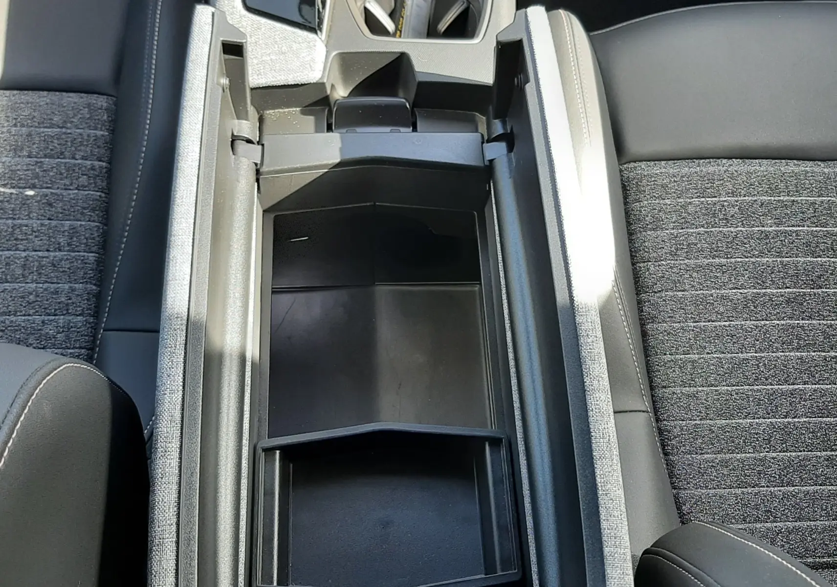 Vue plongeante sur la console centrale ouverte du Peugeot 5008 gris, montrant le rangement intérieur et les sièges tissu gris foncé.