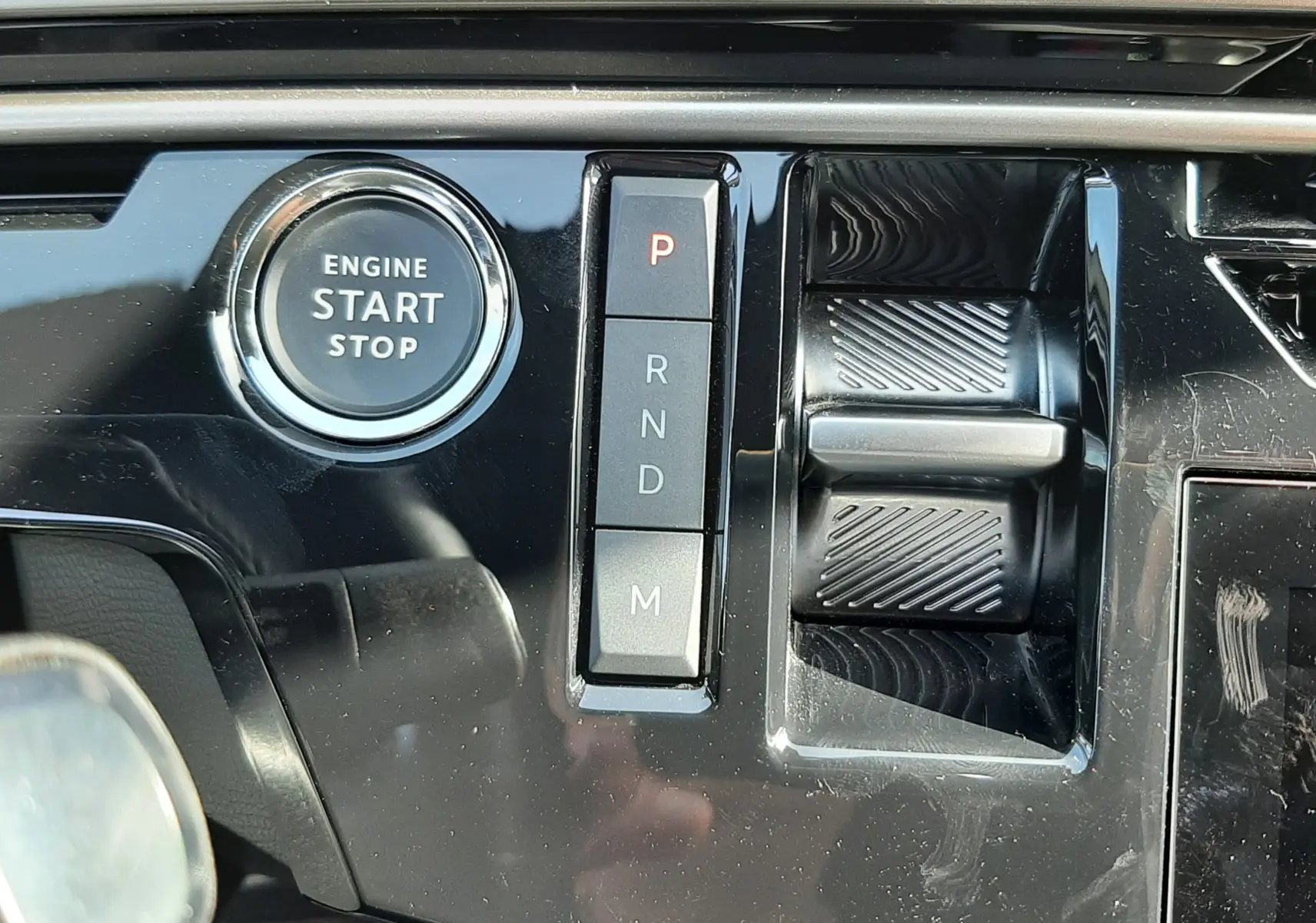 Gros plan sur la console centrale noire brillante du Peugeot 5008 Hybrid 2025, avec bouton start/stop et sélecteur de vitesses automatique.