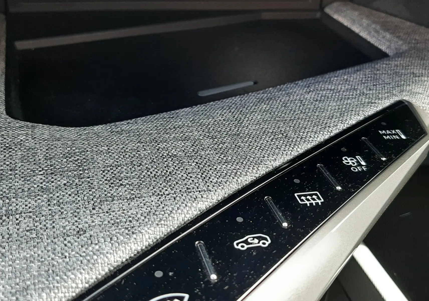 Gros plan sur la console centrale du Peugeot 5008 Hybrid 2025, tissu gris clair et commandes tactiles de climatisation.