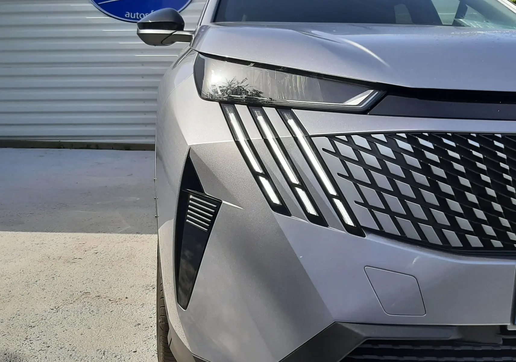 Vue avant gauche rapprochée du Peugeot 5008 gris Artense métal, mettant en valeur ses phares LED distinctifs et sa calandre moderne.