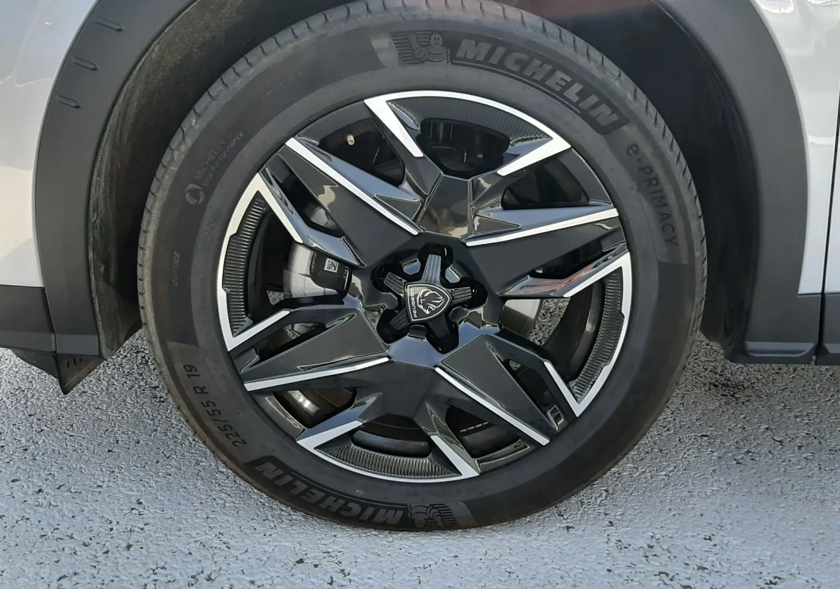 Gros plan sur la roue avant gauche du Peugeot 5008 gris Artense, jante alliage noire et argent avec logo Peugeot central.