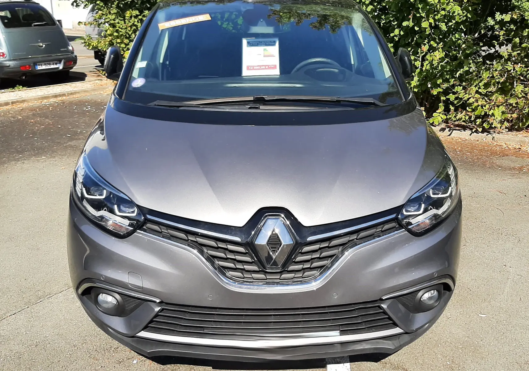 Vue avant d'un Renault Scénic IV gris Cassiopée avec toit noir, calandre marquée et phares LED allumés.