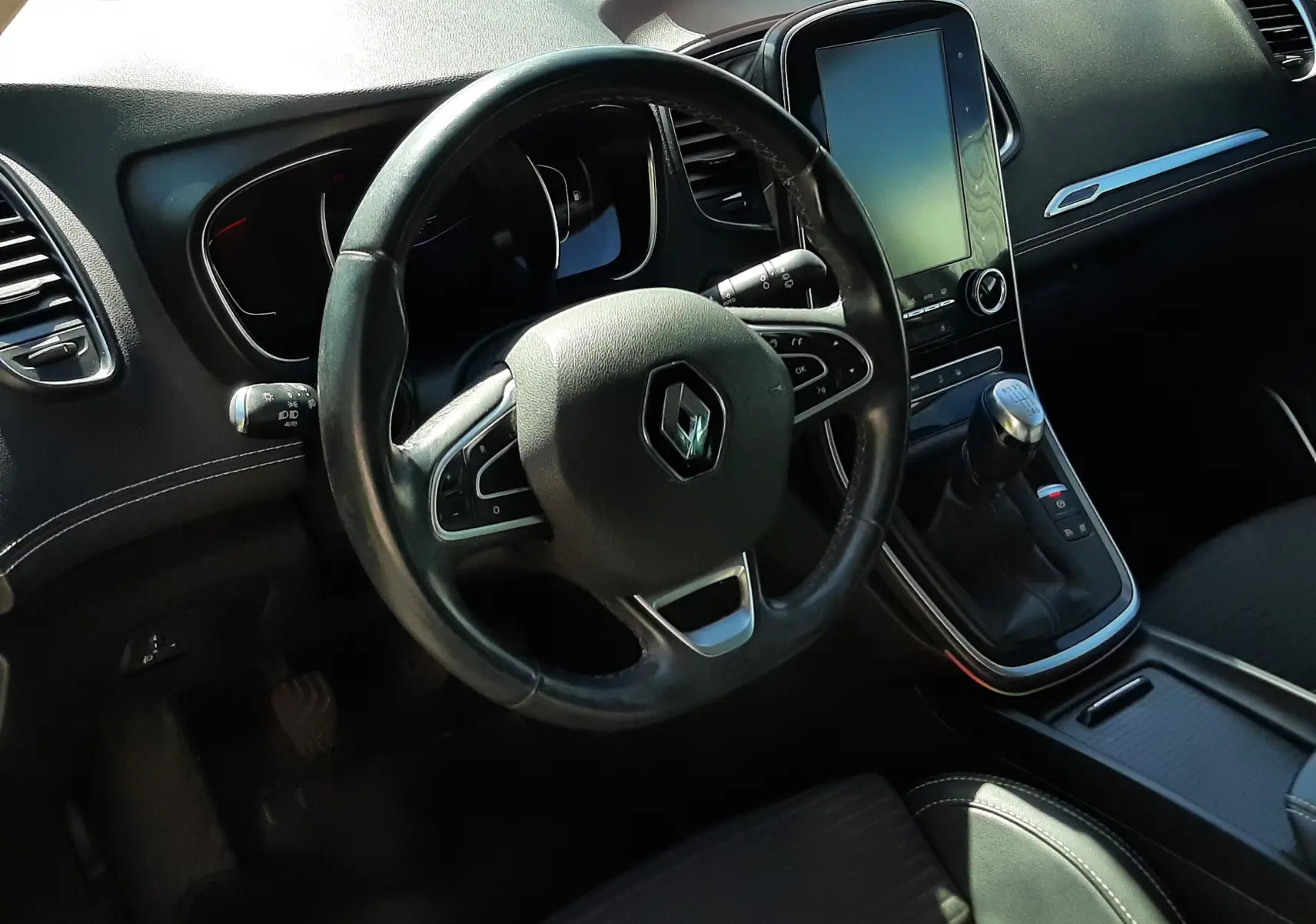Vue intérieure côté conducteur du Renault Scénic IV 2018, volant cuir, écran tactile vertical et levier de vitesses manuel.