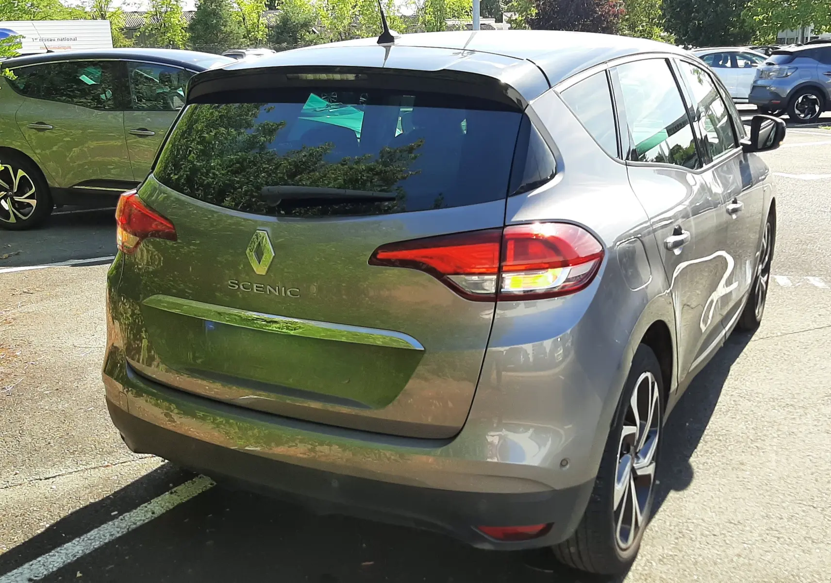 Renault Scénic IV gris cassiopée avec toit noir, vue 3/4 arrière droit, feux arrière allumés, stationné en extérieur.