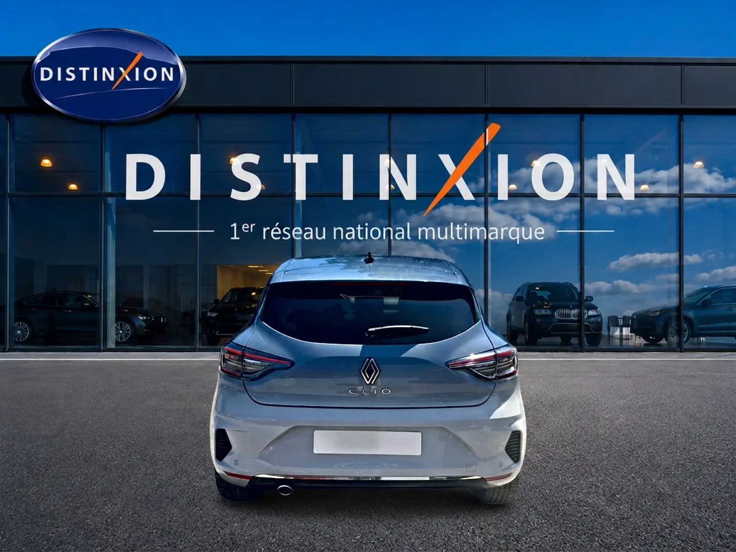 Vue arrière d'une Renault Clio V gris rafale garée devant une vitrine avec logo Distinxion.
