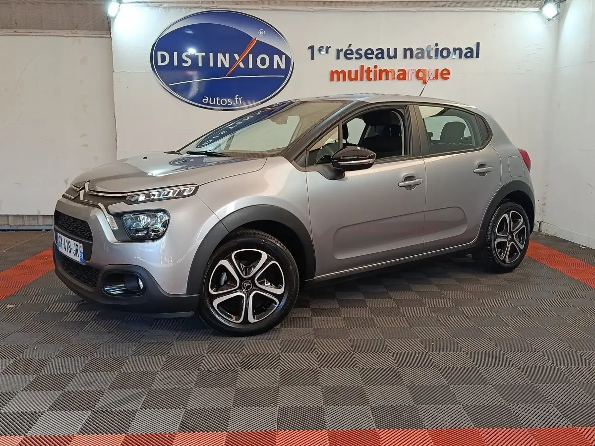 Citroën C3 gris foncé vue 3/4 avant droit, avec phares LED et jantes alliage distinctives en intérieur showroom.