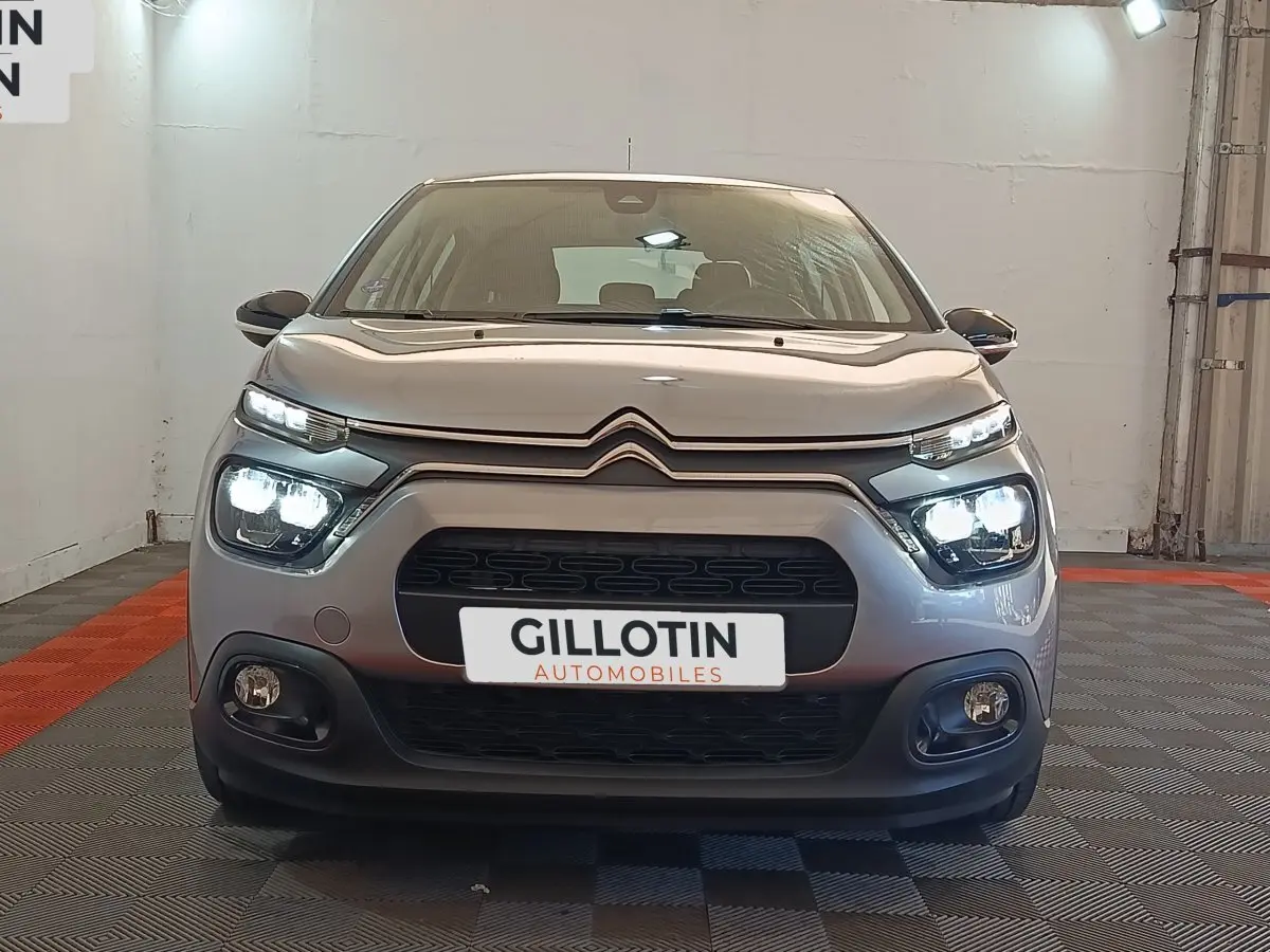 Vue frontale d'une Citroën C3 gris foncé 2024 avec phares LED allumés dans un showroom.