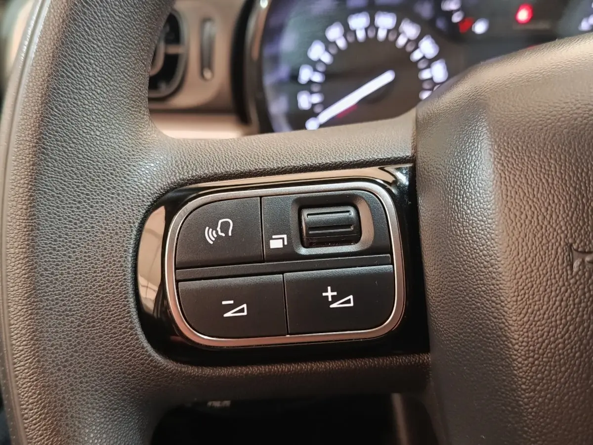 Gros plan sur les commandes multifonctions à gauche du volant d'une Citroën C3 gris foncé, tableau de bord flou en arrière-plan.