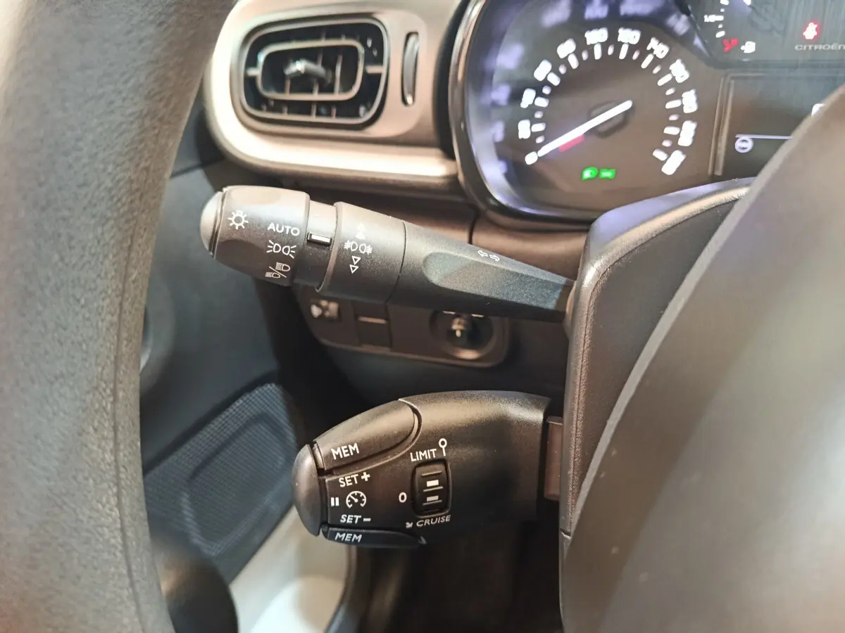 Gros plan sur la commande de régulateur de vitesse et des feux, tableau de bord partiellement visible d'une Citroën C3 2024.