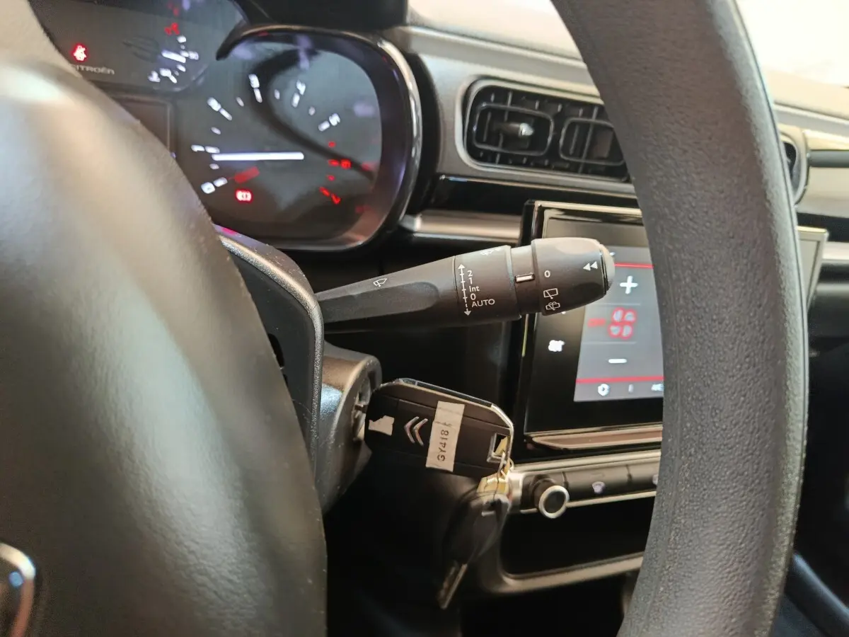 Vue intérieure rapprochée du volant et du tableau de bord d'une Citroën C3 gris foncé avec écran tactile et clé insérée.