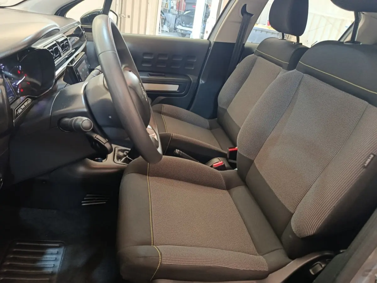 Vue intérieure côté conducteur de la Citroën C3 2024, sièges gris foncé avec surpiqûres jaunes et tableau de bord moderne.