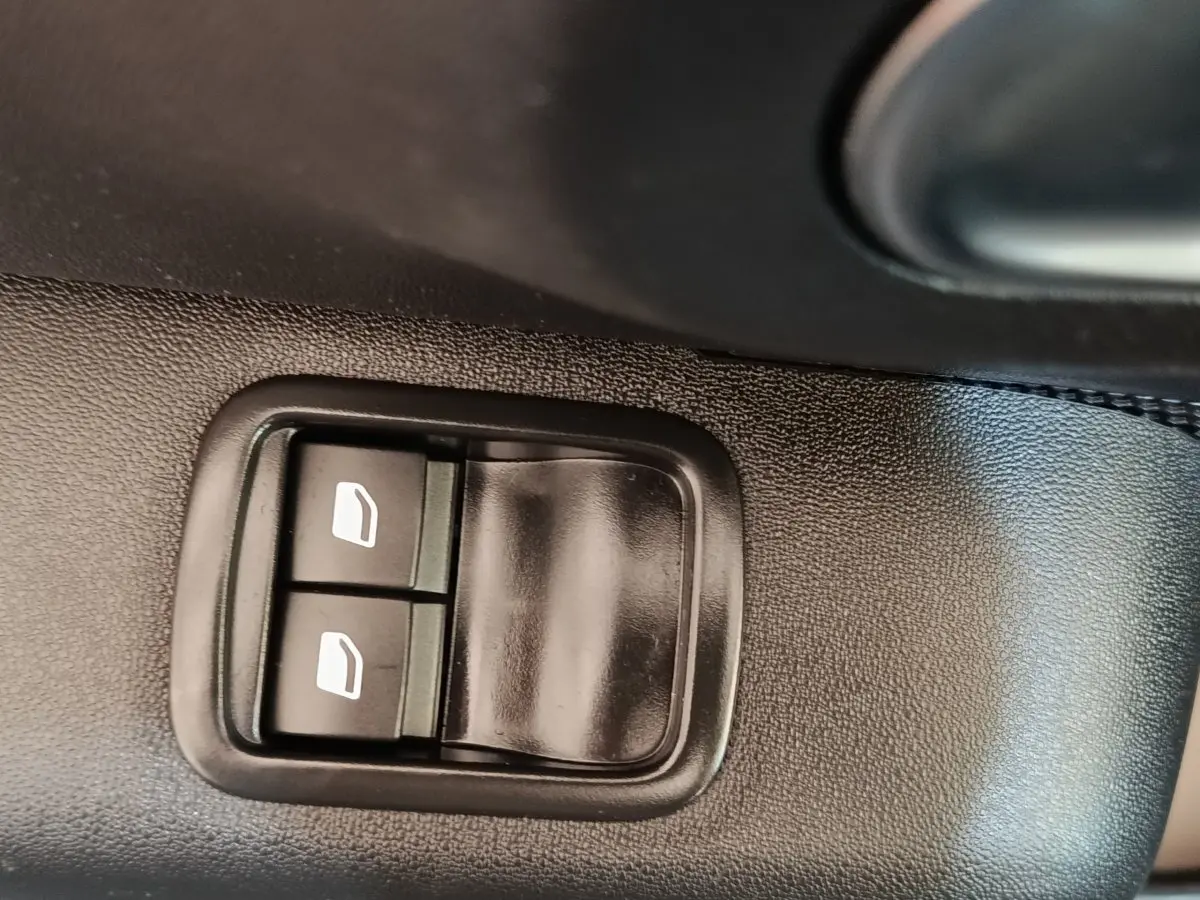 Gros plan sur les commandes des vitres électriques côté conducteur d’une Citroën C3 gris foncé, intérieur voiture.