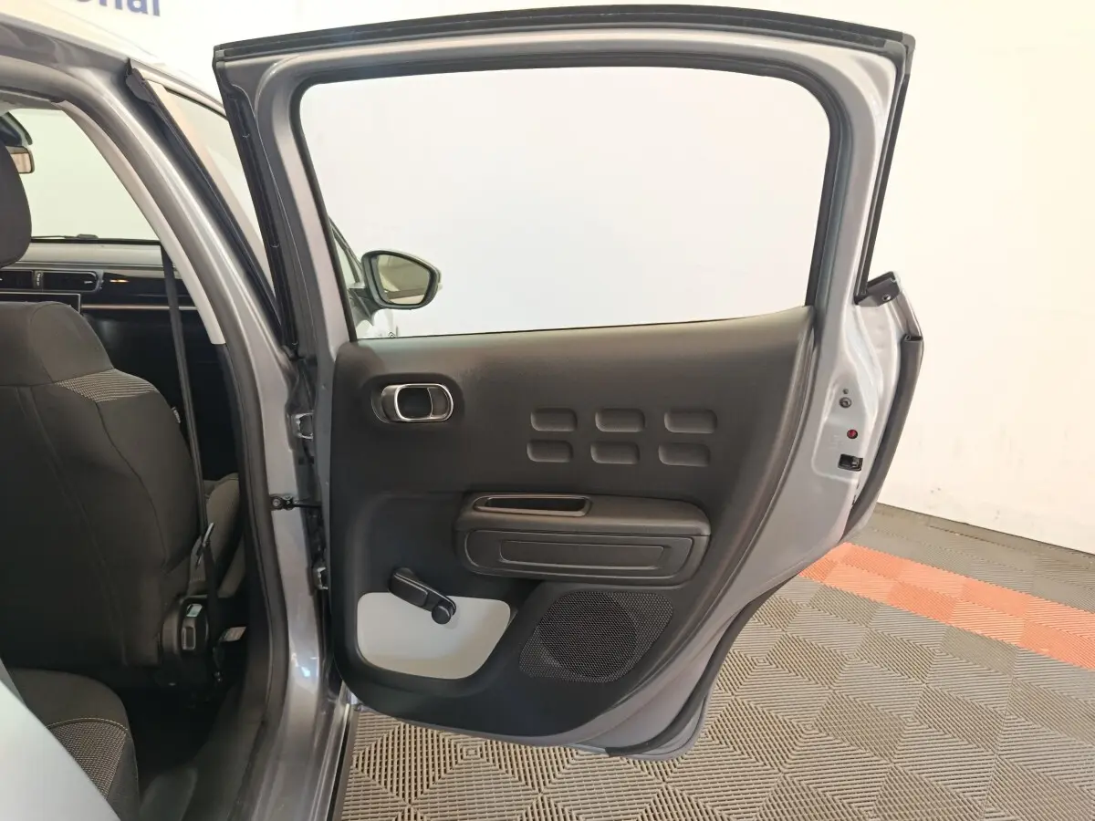Vue intérieure côté gauche de la porte arrière ouverte d'une Citroën C3 2024 gris foncé, avec manivelle de vitre visible.