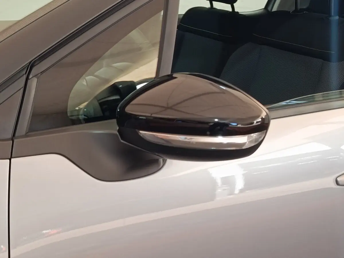 Gros plan sur le rétroviseur noir brillant côté gauche d'une Citroën C3 gris foncé avec partie de la porte visible.