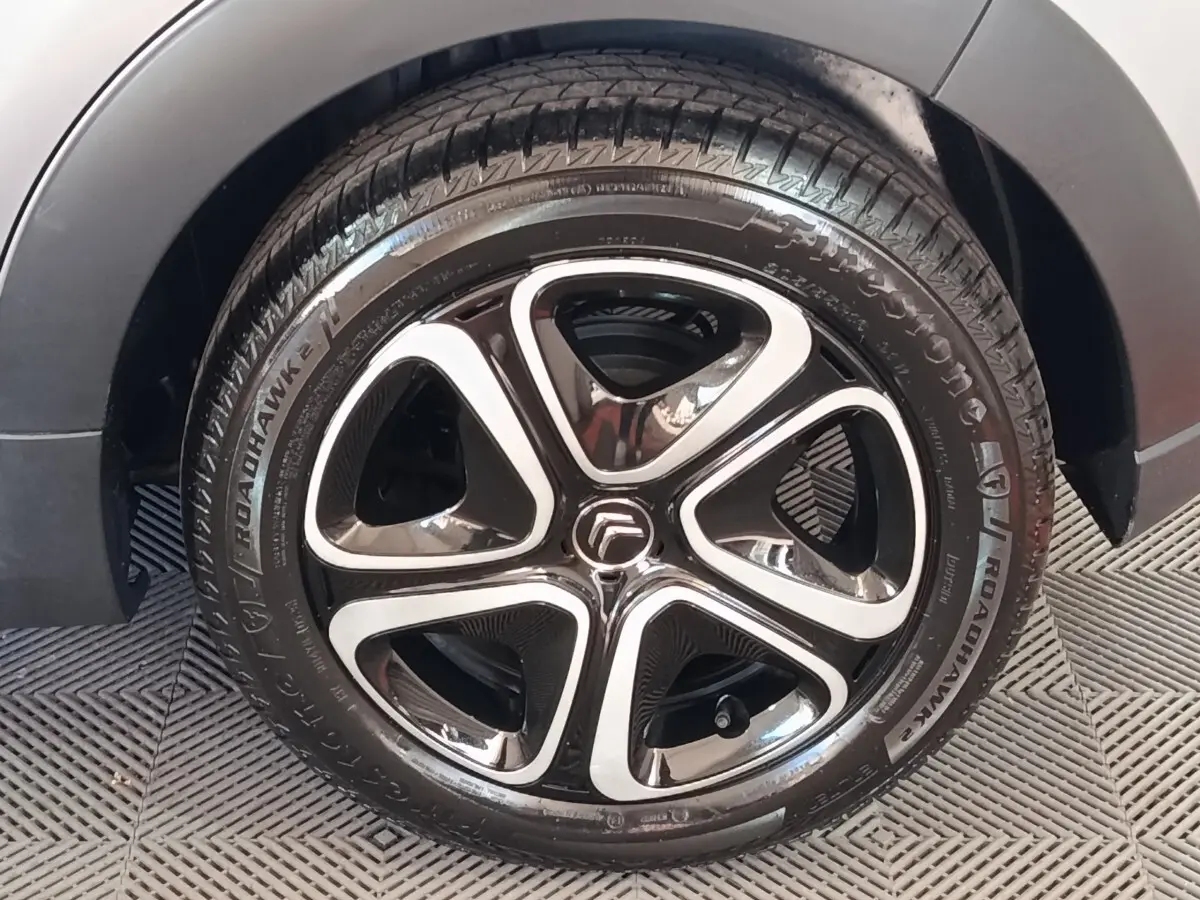Gros plan sur la roue avant droite d'une Citroën C3 gris foncé avec jante alliage noire et argentée.
