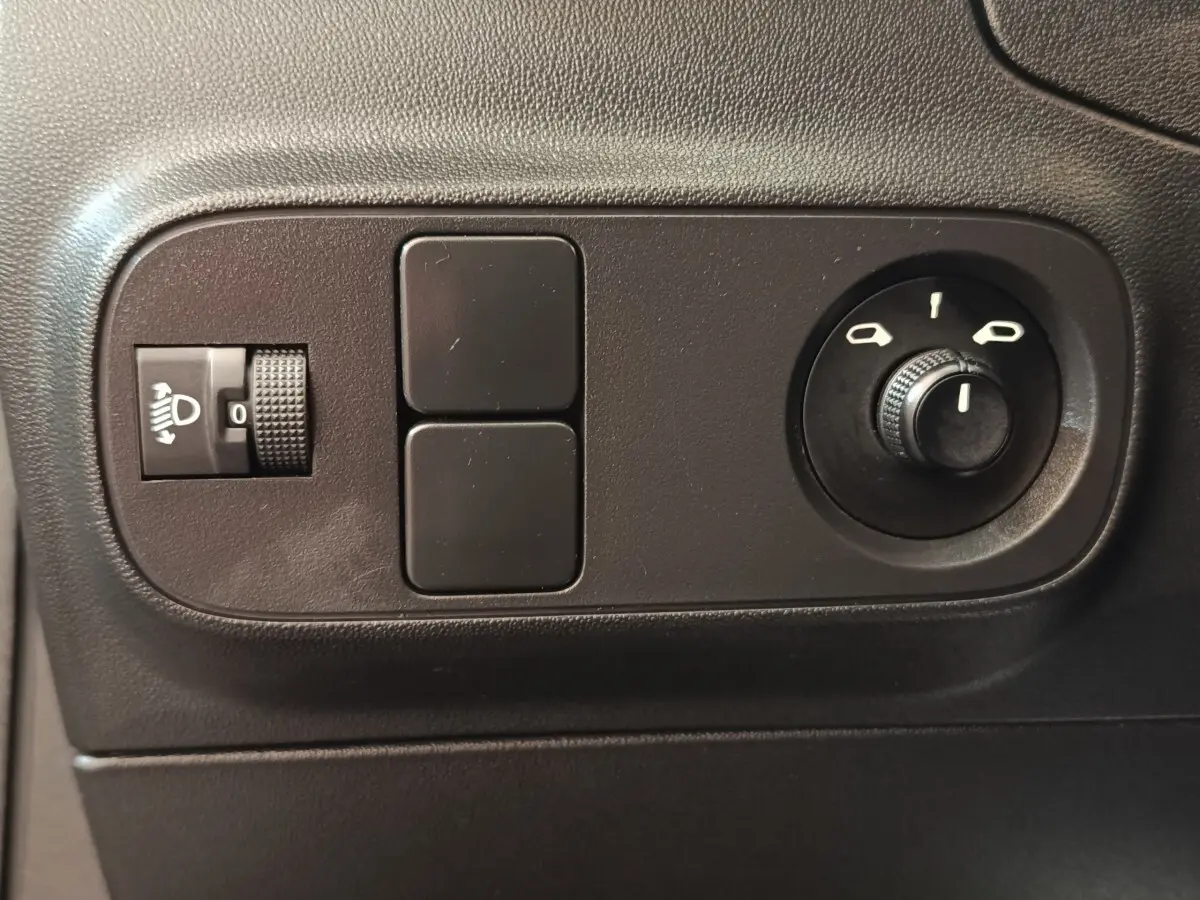 Gros plan sur les commandes noires de réglage des phares et des rétroviseurs dans une Citroën C3 gris foncé 2024.