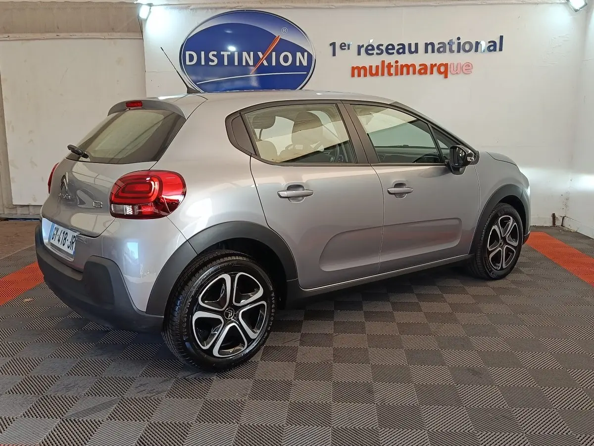 Vue 3/4 arrière droite d'une Citroën C3 gris foncé 2024 avec jantes noires et rouges, stationnée en intérieur.