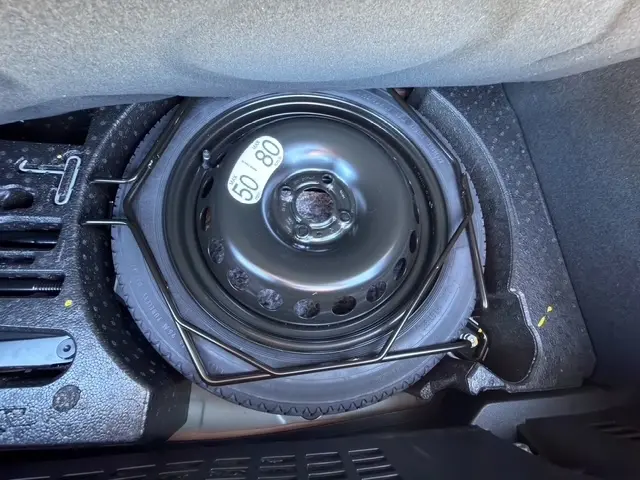 Roue de secours noire avec étiquette de limitation de vitesse, rangée dans le coffre d'une Renault Clio gris clair 2025.