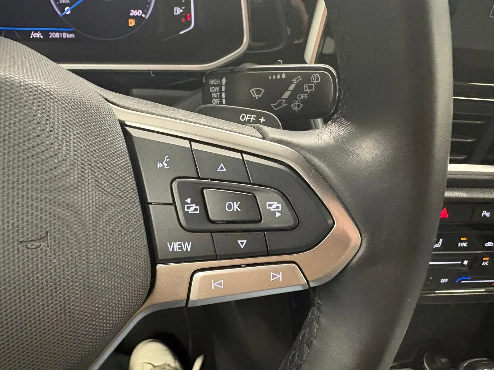 Gros plan sur les commandes gauche du volant cuir du Volkswagen T-Roc 2024 bleu pétrole avec affichage numérique.